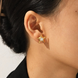 Close-up of golden star stud earring with white enamel inlay worn on ear