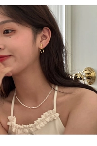 Dettaglio di orecchini a fiocco dorati e collana di perle indossati da una modella