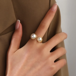 Close-up of golden open ring with dual white pearls on hand against brown suit jacket