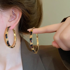 Model wearing large golden hoop earrings with leopard print detail and a vintage style