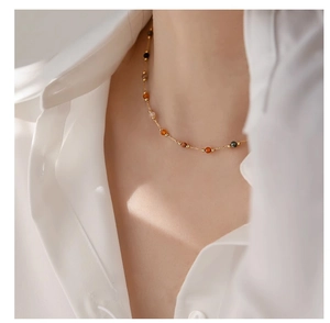 Detail of a thin gold necklace with colorful natural stone beads on a white shirt
