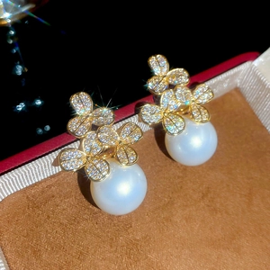 Detail of gold flower earrings with pavé crystals and dangling round white pearl
