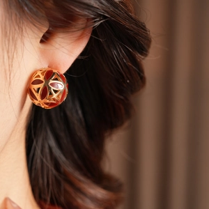 Détail de boucles d'oreilles vintage rondes dorées avec motif floral rouge sur modèle