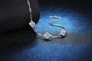 Macro detail of silver four-leaf clover pendant with pavé-set stones on paperclip chain