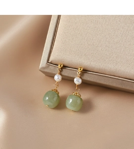 Macro detail of vintage earrings featuring white pearls and green jade beads on gold silk