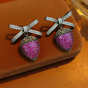 Macro detail of strawberry earrings with cubic zirconia bow on brown velvet jewelry box