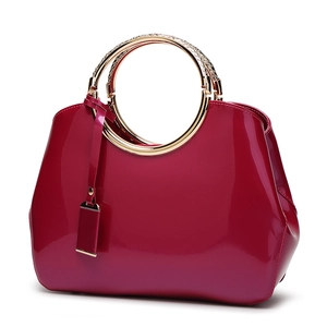 Glossy magenta patent leather handbag with textured golden metal ring handles