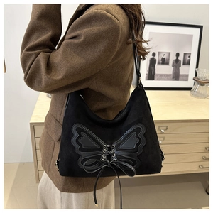 Winter black suede tote bag with large butterfly bow design shown on model's shoulder