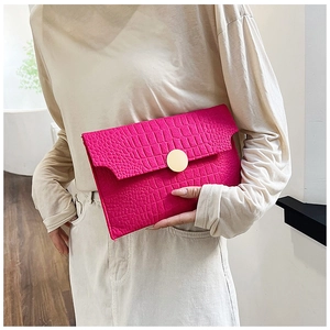 Detail of fuchsia crocodile texture envelope clutch bag with gold round metal buckle clasp