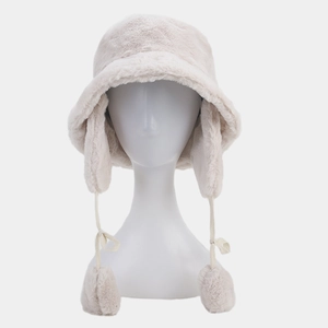 Close-up of beige plush bucket hat with long earflaps and decorative pom-poms