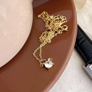Detail of a gold four-prong zircon pendant necklace on a brown ceramic plate