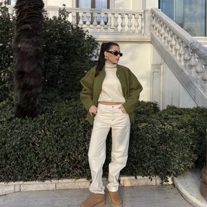 Detail of olive green knit cardigan styled with a white turtleneck and beige straight pants