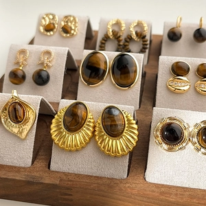 Gold-plated tiger eye geometric earrings collection on a grey wooden jewelry display