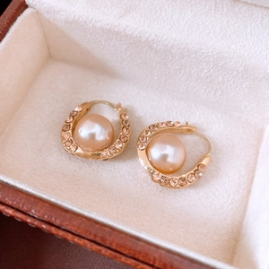 Detailed close-up of gold U-shaped earrings with champagne pearl and pavé rhinestones