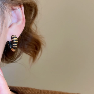 Vue détaillée de créoles torsadées en or 18k et noir portées à l'oreille d'un modèle