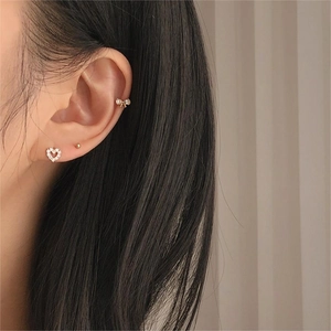 Close-up of model wearing gold heart studs, ball earrings, and bow ear cuff set