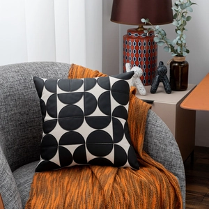 Close-up of geometric black leather and fabric pillow on a gray chair with orange throw