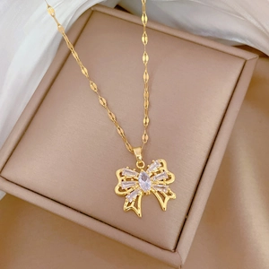 Elegant gold bow necklace with crystal zircons displayed on a beige jewelry box