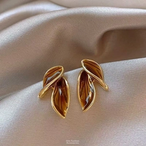 Macro view of vintage gold-plated leaf earrings on elegant champagne silk fabric