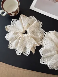 Detail of beige lace embroidery scrunchie with scalloped edges on a dark wood surface