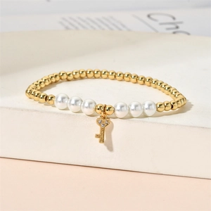 Close-up of beaded pearl bracelet with gold beads and a sparkling diamond key pendant