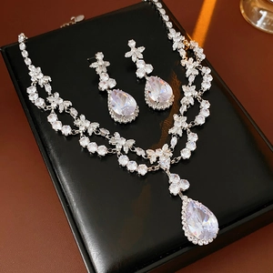 Macro shot of silver zircon flower teardrop pendant necklace and earrings on black leather