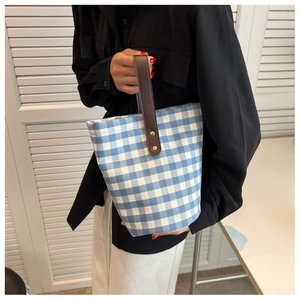 Detail of blue and white checkered bucket bag with brown leather handle and metal rivets