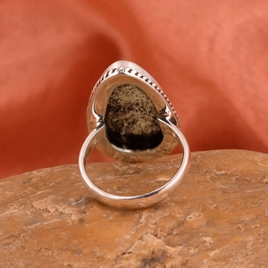 Macro de anillo de plata con piedra natural sobre roca y fondo de tela roja vibrante