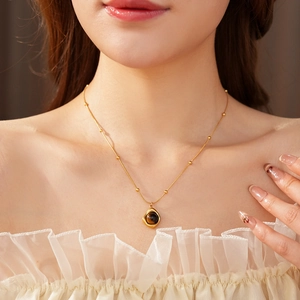 Close-up of golden beaded chain with an irregular tiger eye stone pendant on a model