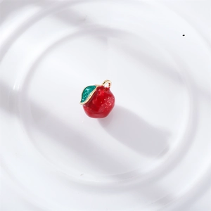 Detail of a red enamel apple charm with gold ring and green leaf for DIY jewelry making