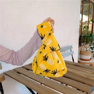 Japanese style yellow canvas wrist bag with pineapple pattern on a wooden table