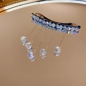 Detail view of gold hair clip with sparkling crystal fringe on a mirrored background