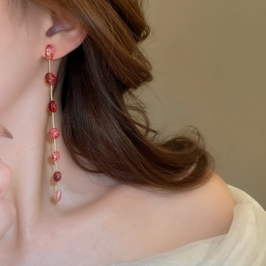 Close-up of strawberry crystal tassel earrings with long gold chains on female model