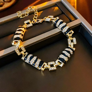 Adjustable gold bracelet with black enamel accents and sparkling rhinestones on tray