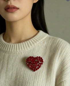 Close-up of heart-shaped brooch with deep red crystals on silver base on knit sweater