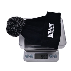 Detailed shot showing the 99.3g weight of the knitted MOMMY beanie on a digital scale