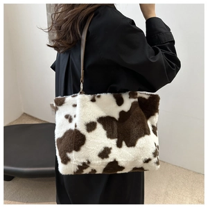 Brown and white cow print plush shoulder bag shown on model in a modern interior