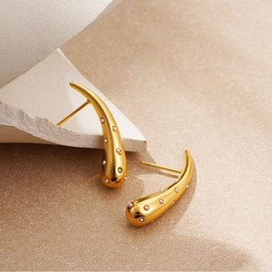 Detail view of 18K gold teardrop earrings with inlaid white pearls on a stone surface