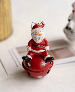 Close-up of resin Santa Claus sitting on a red metal bell ornament with star cutouts