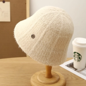 Beige knit bucket hat with vertical texture and metal logo on a wooden stand