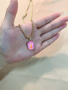 Detail of a gold rope chain necklace with a rectangular pink iridescent gemstone pendant