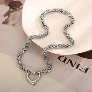 Detail of silver heart pendant with thick byzantine chain necklace on a ceramic plate