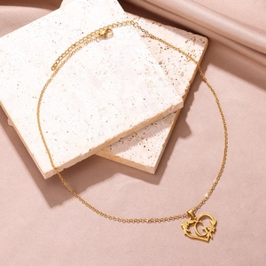 Dettaglio pendente a cuore dorato con lettera G e motivi floreali su seta rosa