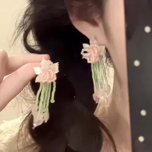 Detail view of floral tassel earrings with pink flower petals and green fringe tassels