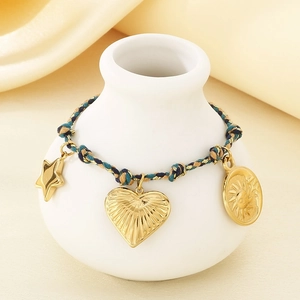 Detailed shot of braided cord bracelet with gold sun and heart charms on a ceramic vase