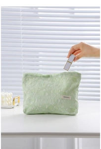 Close-up of light green jacquard toiletry bag with hand putting lipstick inside