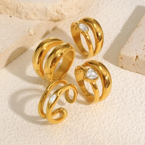 Elegant gold stainless steel layered rings with clear zircon stones on textured stone background