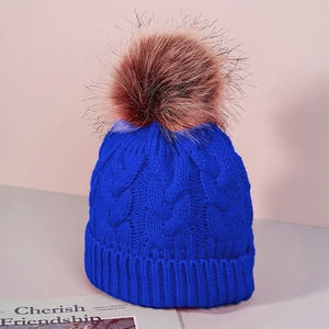 Detail of royal blue cable knit winter hat with large brown faux fur pompom and ribbed cuff