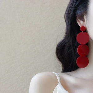 Macro shot of tiered red acrylic circular drop earrings styled on a fashion model