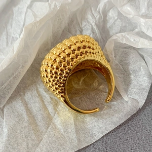 Detailansicht verstellbarer goldener Ring mit Kugelstruktur auf weißem Papiergrund